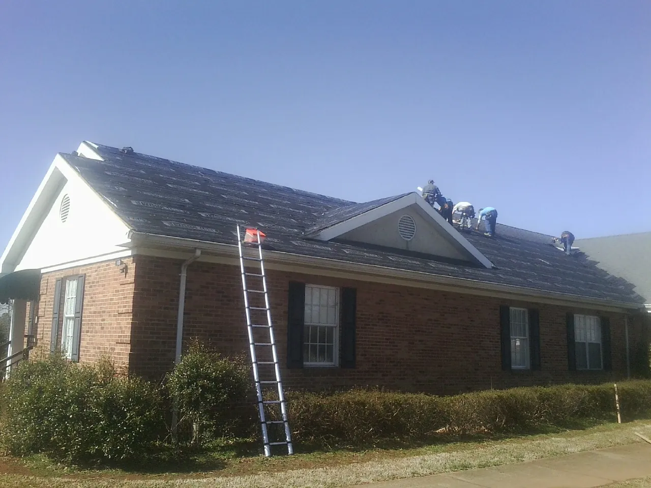 Crew tearing shingles off a brick ranch roof with a ladder set — Emergency Roof Repair work by our crew in Greene