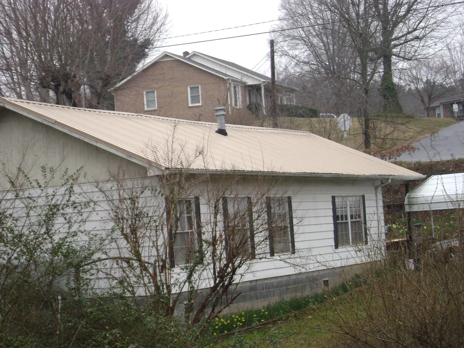 Tan metal roof on a white sided house set into a hillside — Commercial Roofing by Roofing Brothers in Greene